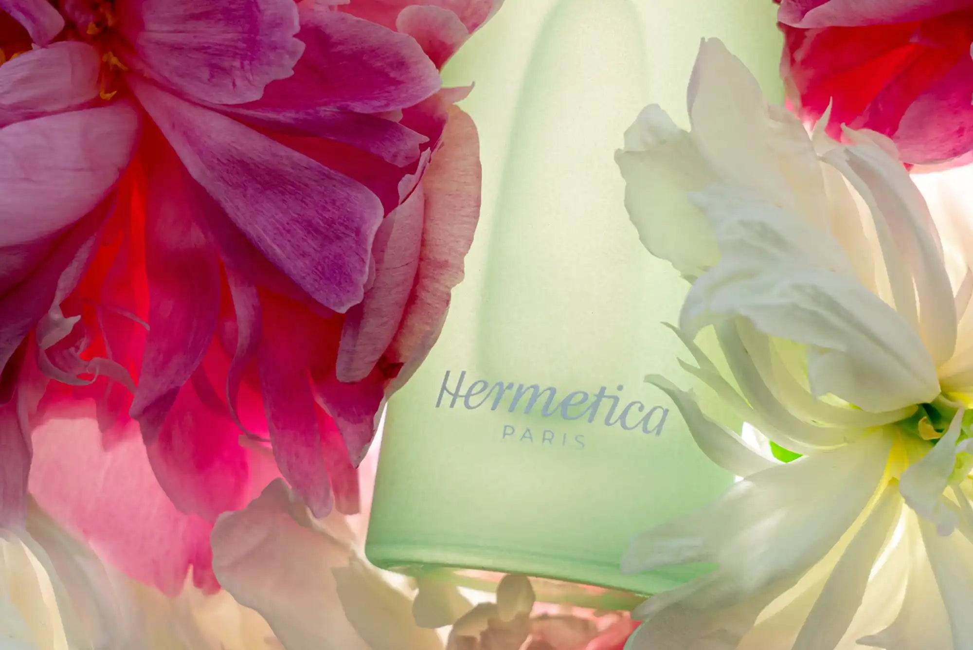 Frosted glass bottle labeled ’Hermetica’ surrounded by pink and white flowers.