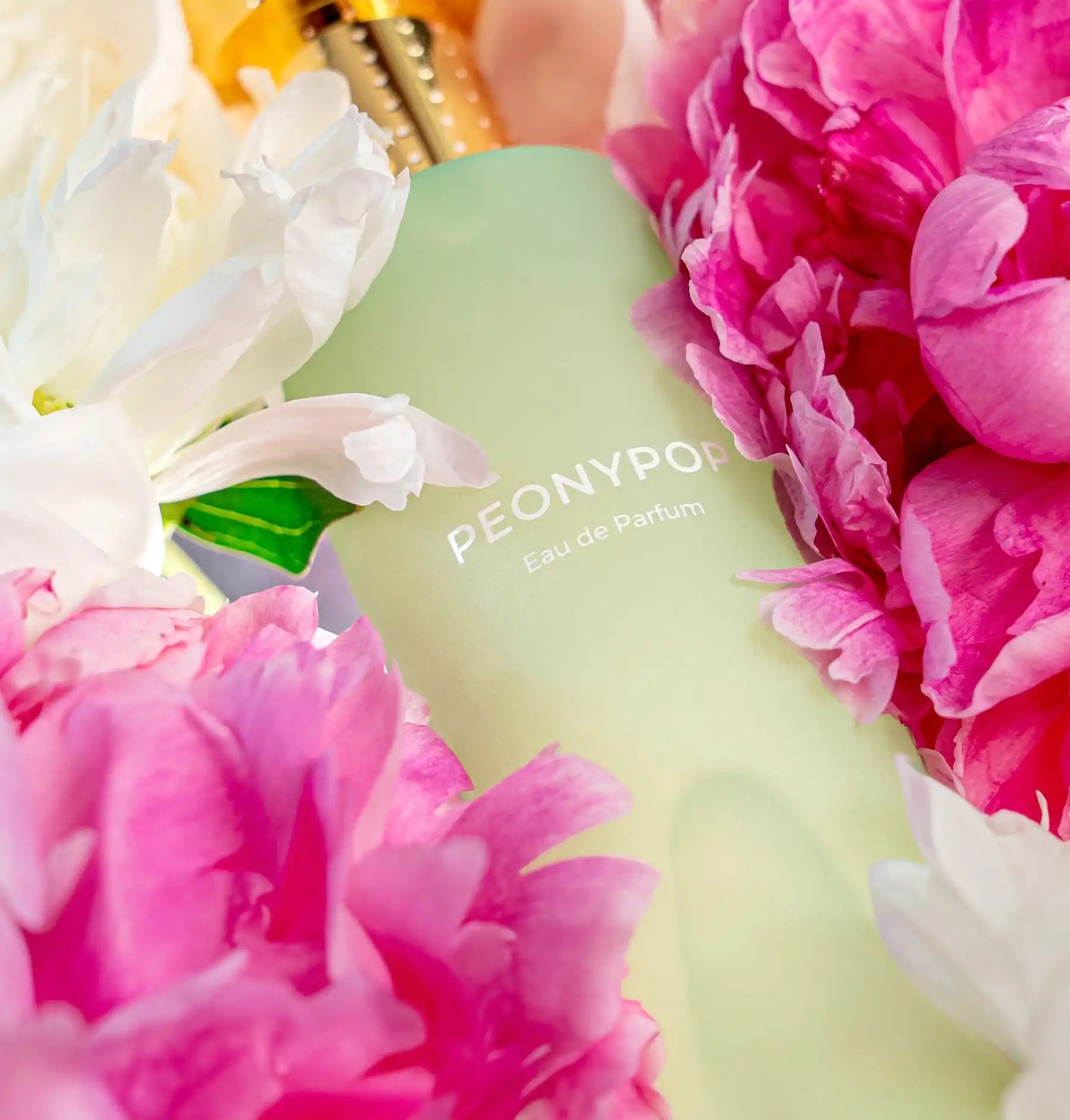 Frosted green glass bottle labeled ’Peony’ surrounded by pink and white peony flowers.
