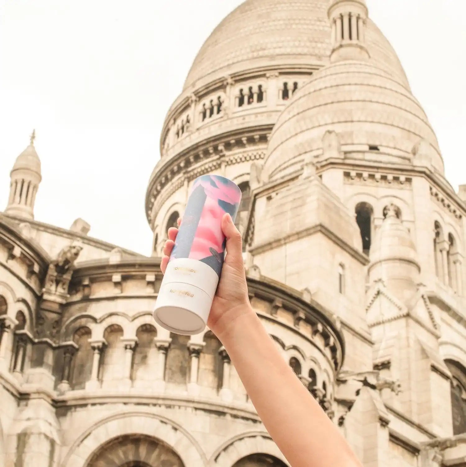 Hand holding a pink beverage can against the Sacré-Cœur Basilica in Paris.