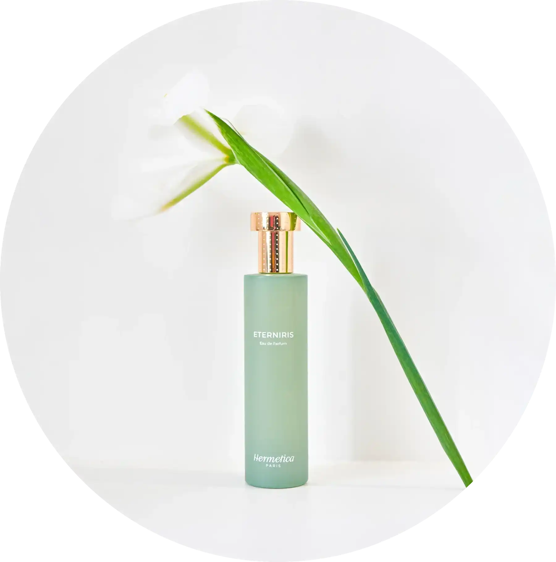 Mint green glass perfume bottle with a gold cap and a bamboo leaf beside it.