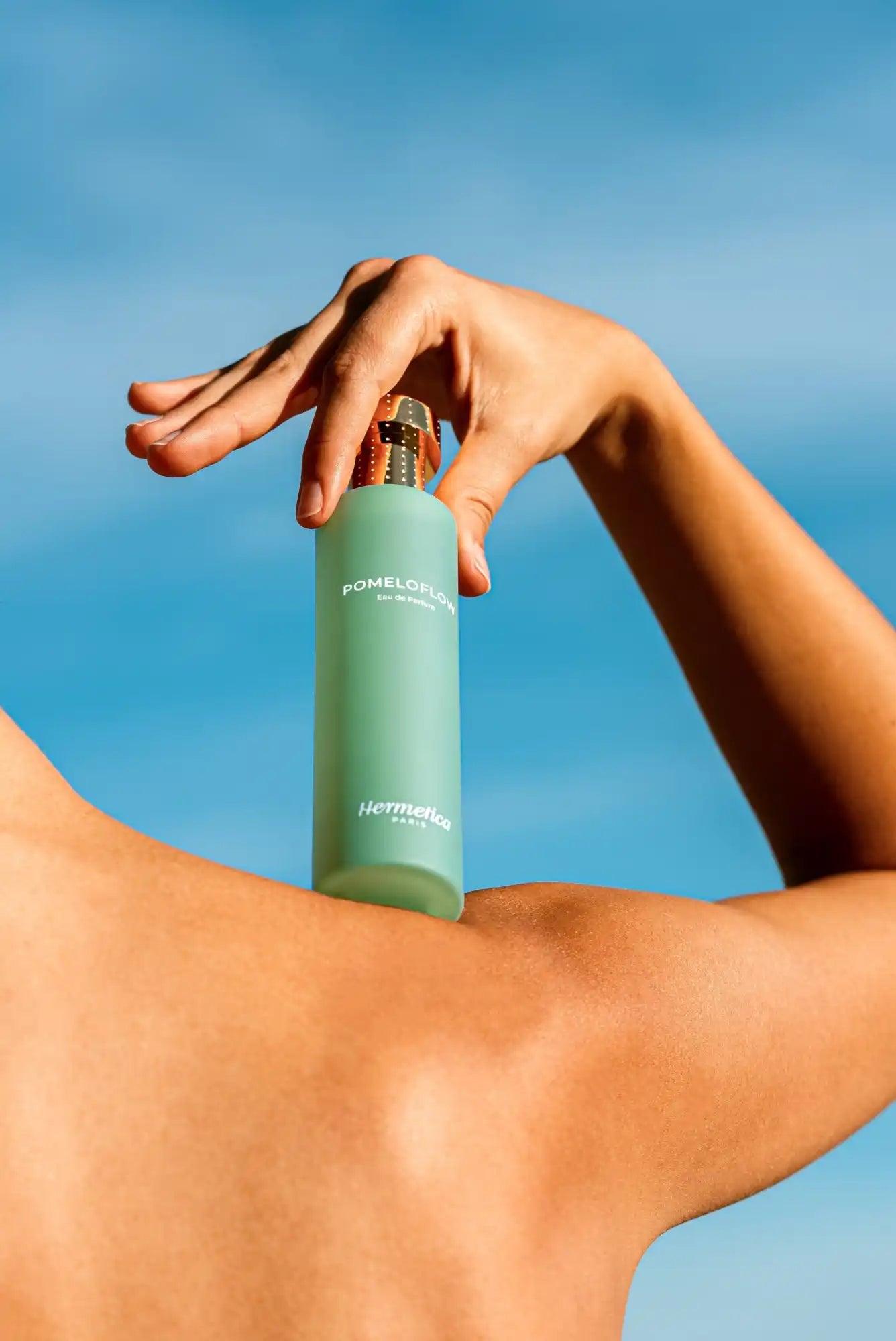 A teal-colored cylindrical bottle being held by a hand against a bare shoulder.