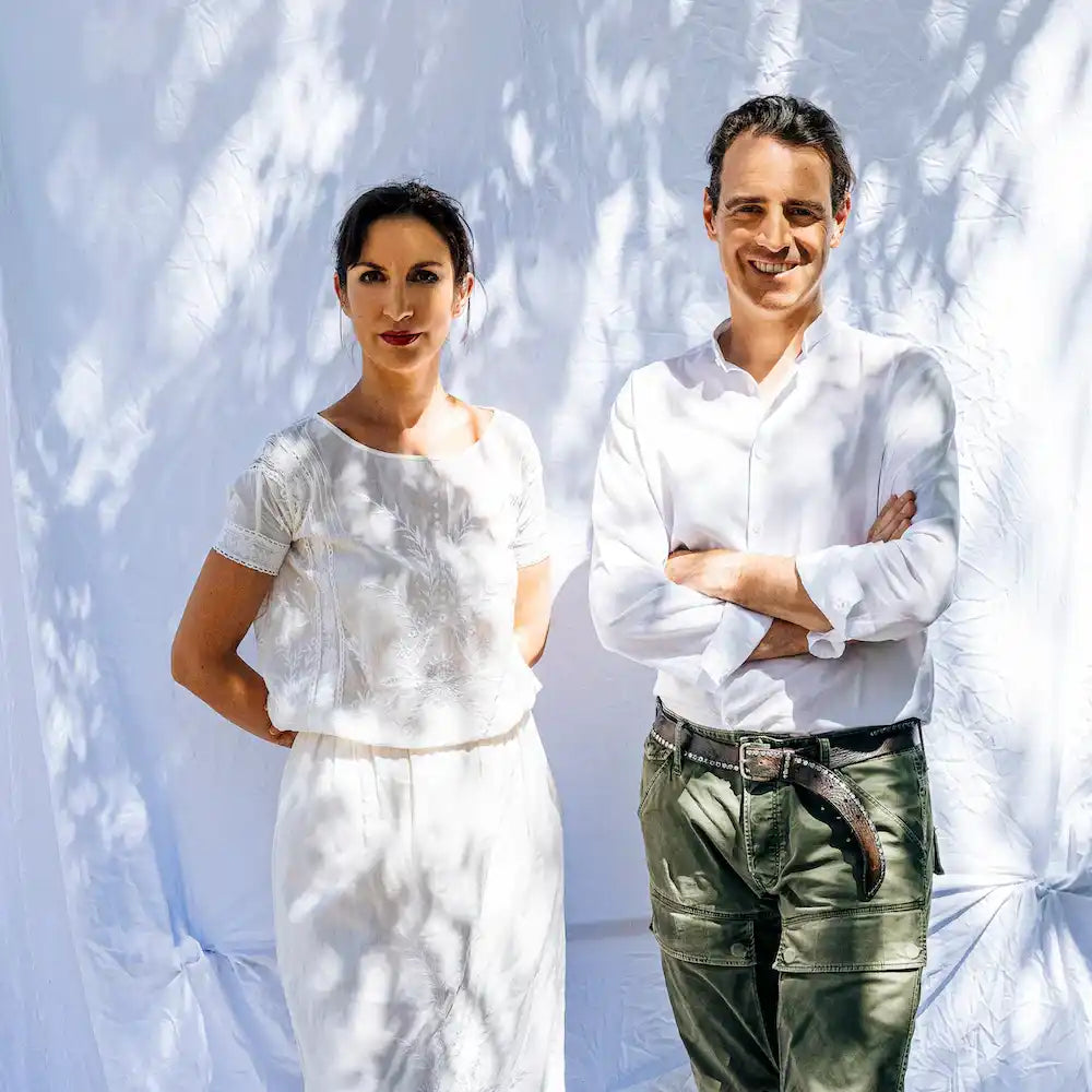 Two people wearing white tops standing against a wall with dappled shadows.